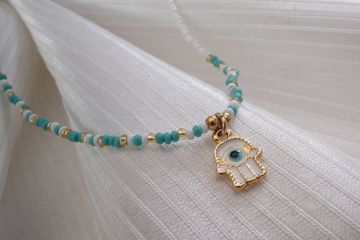 Bracelet with turquoise and gold beads and a hamsa hand charm on a white fabric background